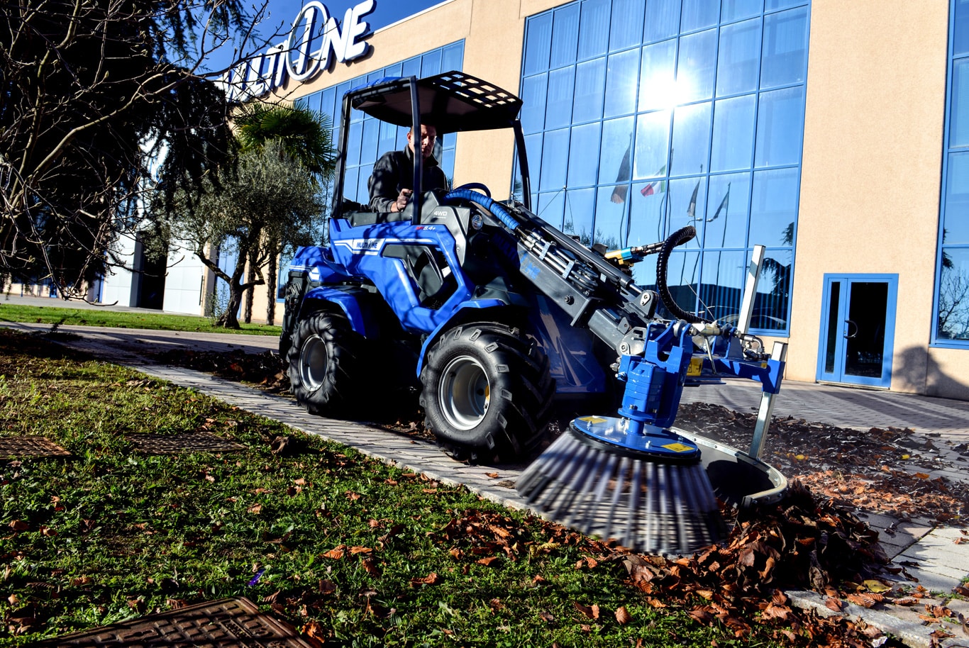 mini loader with a side brush attached, cleaning leaves in front of multione venue