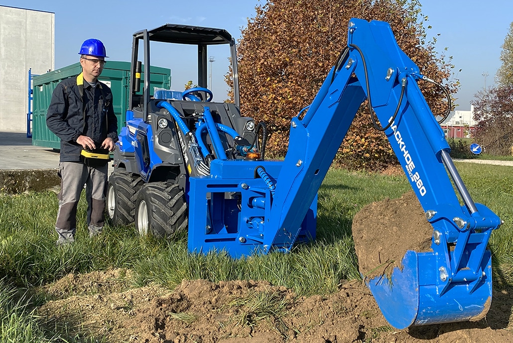 A worker radio controlling the backhoe assembled on a mini loader, viewed from the front