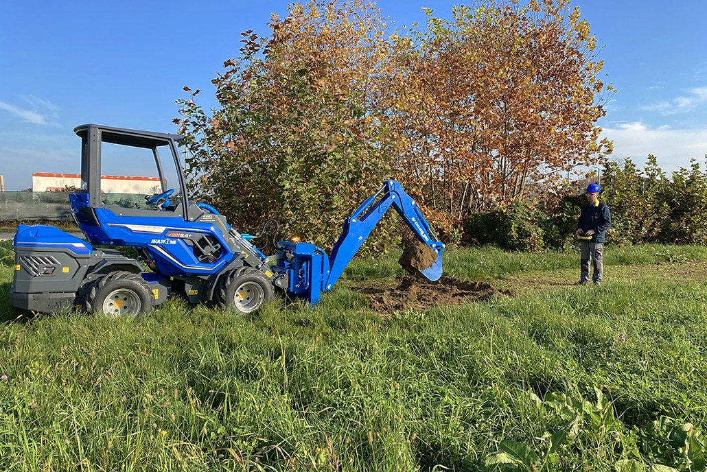 A worker radio controlling the backhoe assembled on a mini loader, viewed from afar