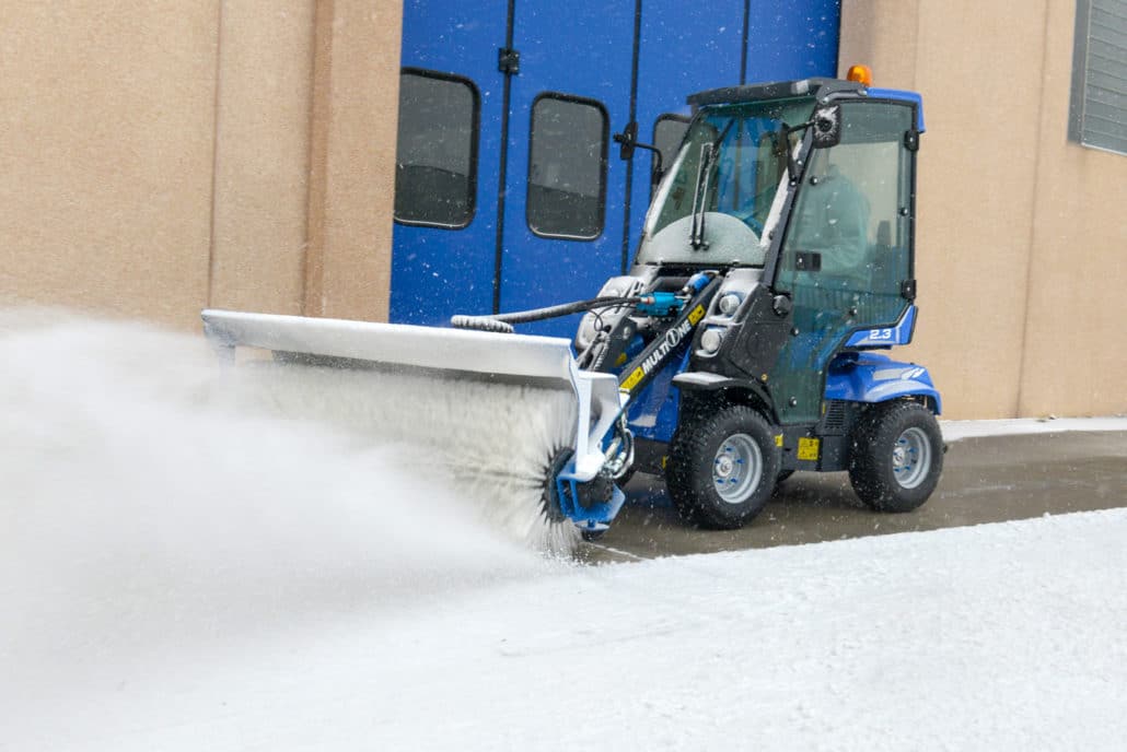 a mini loader 2 series with rotary broom cleaning a street