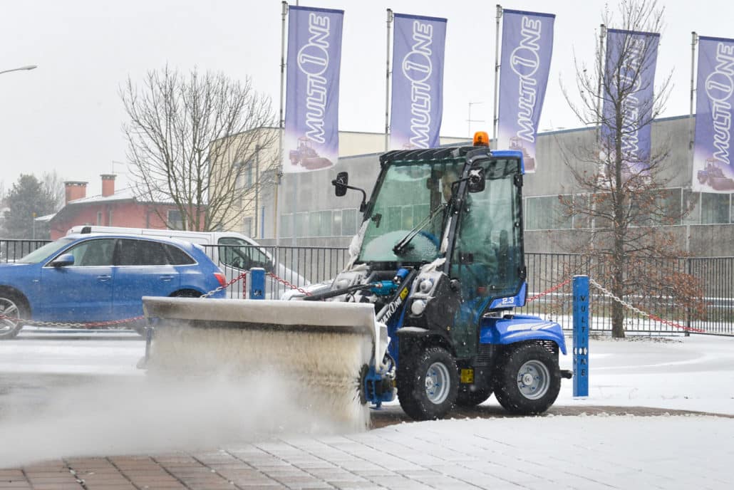 a mini loader 2 series with rotary broom cleaning a snowy pavement in front of multione venue