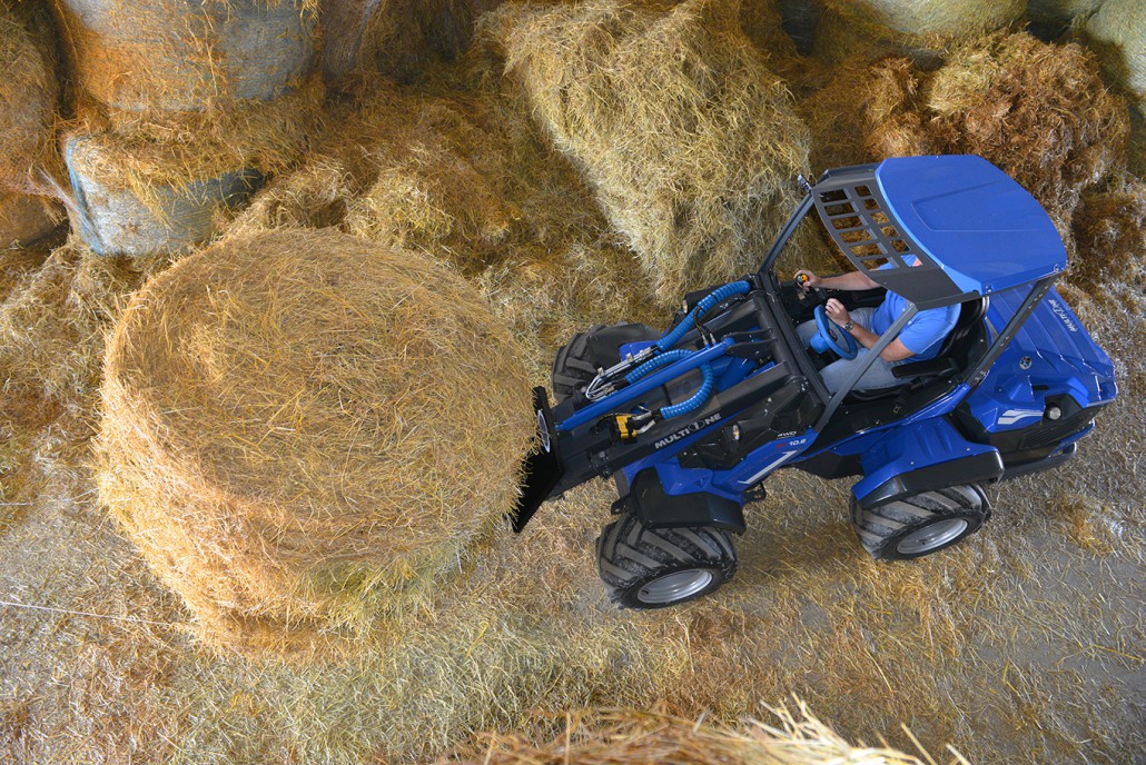 man using a bale fork to lift a big hay bale, upper view