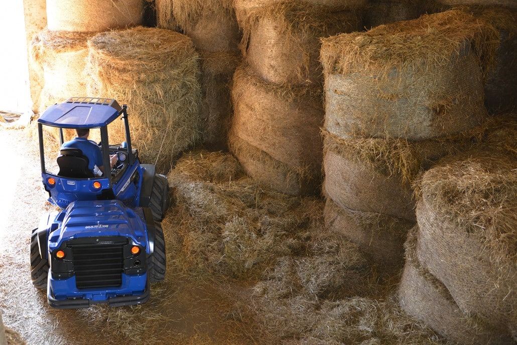 man using a bale fork to lift a big hay bale, upper view from behind