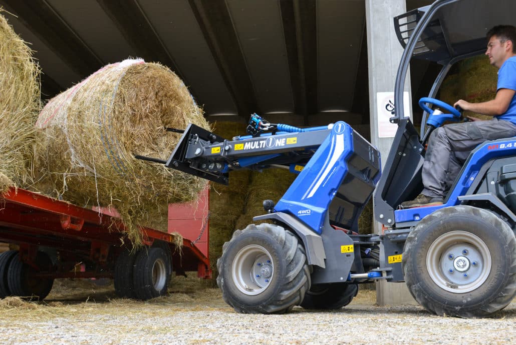 man using a bale fork to lift a big hay bale, rear view