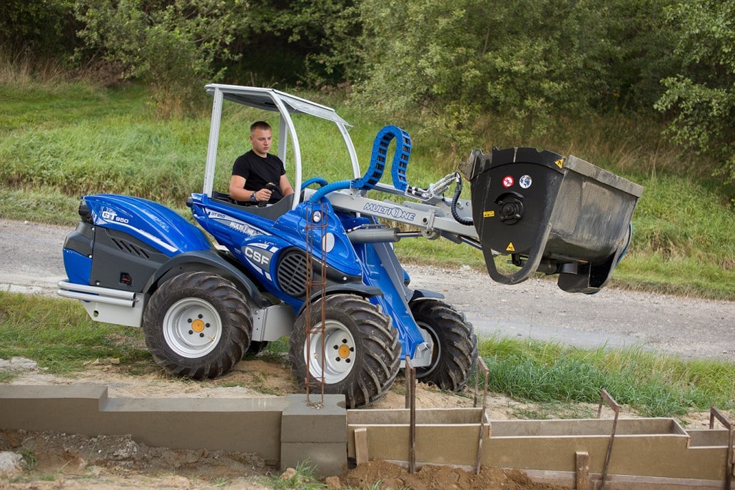 man driving a mini loader with a concrete mixing bucket