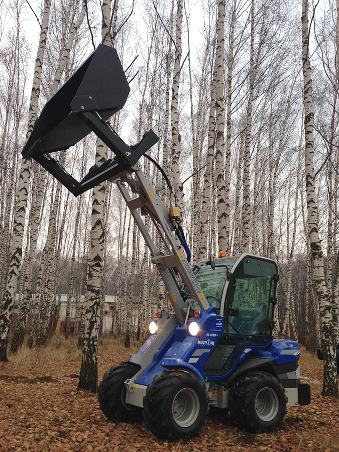 high tip bucket with lifted boom, in a forest