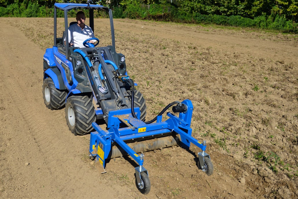 worker driving a mini loader with power rake on soil