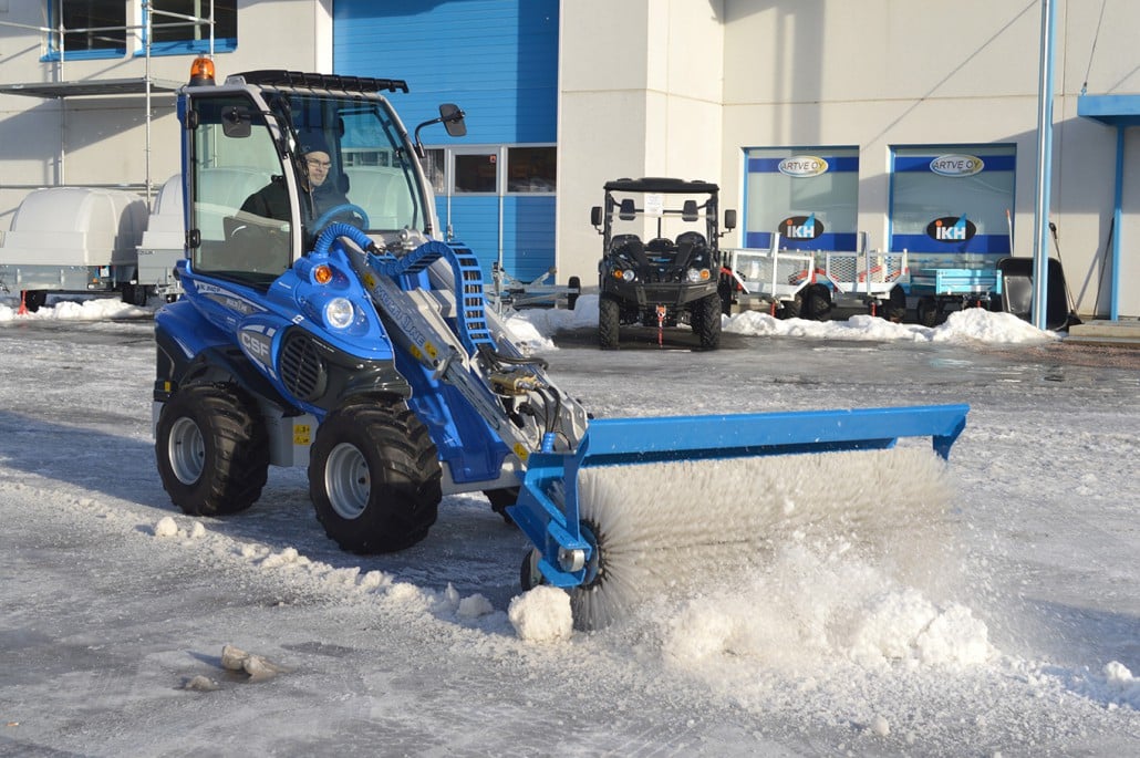 a man driving a mini loader with rotary broom in a machinery fleet